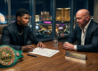Photo of boxer Shakur Stevenson signing a contract at a conference table opposite Dana White. A WBC championship belt sits on the table. A Las Vegas skyline is visible through the window.